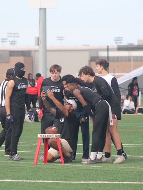 Group of young men huddle around a football on a football field. They are wearing athletic gear and looking at the ball.