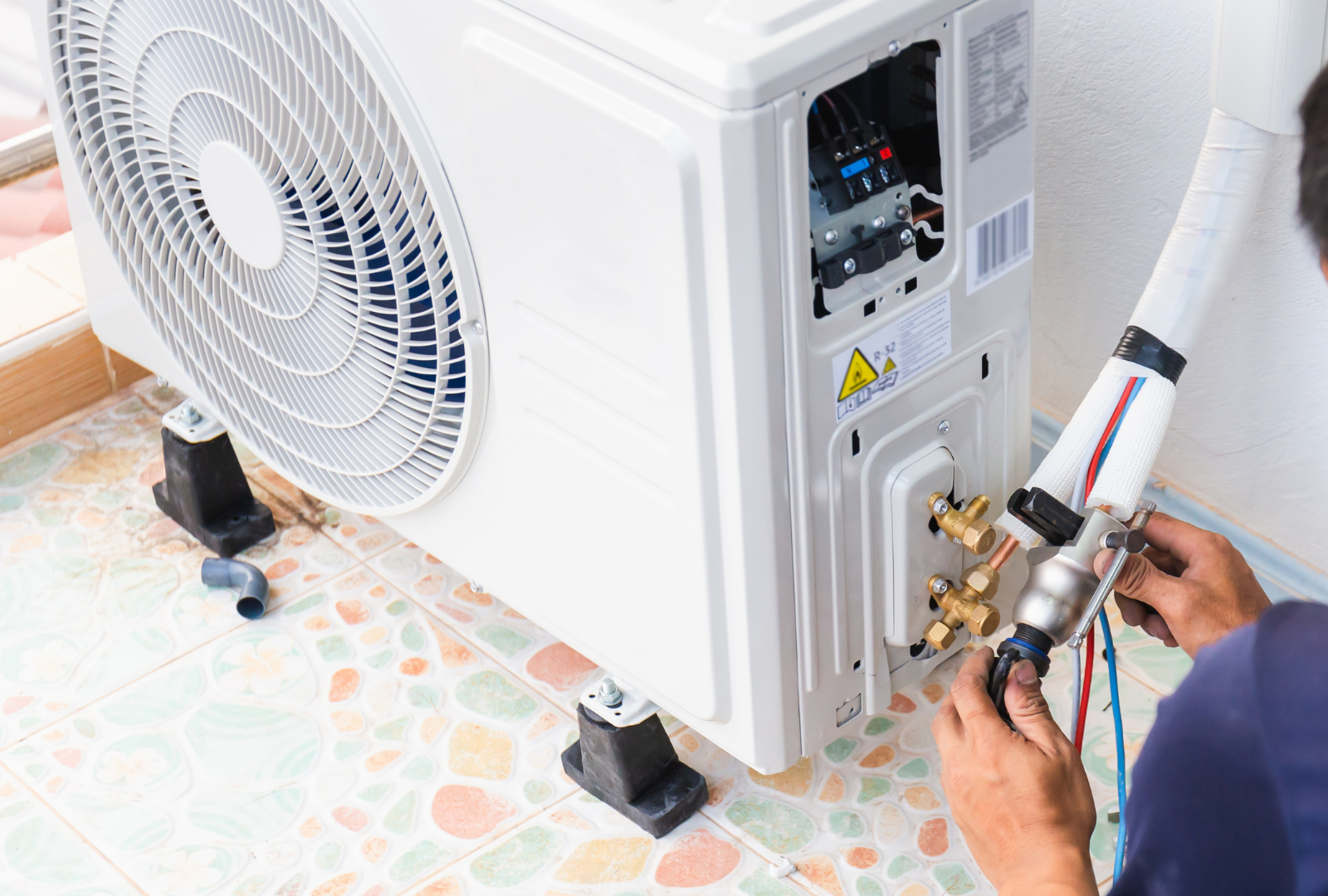 Technician repairing an outdoor air conditioner unit with tools and wires exposed