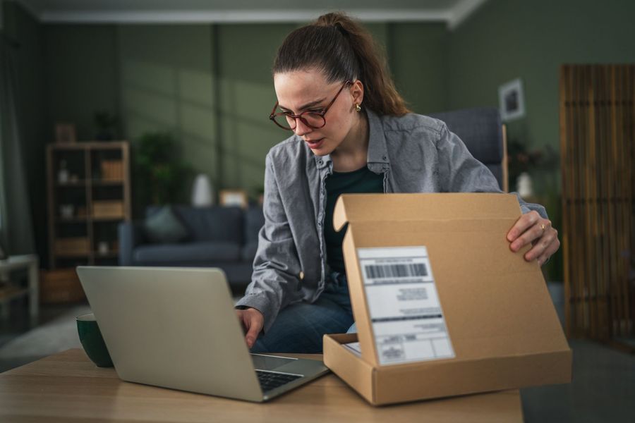 Woman packing a shipping box beside a laptop in a home office