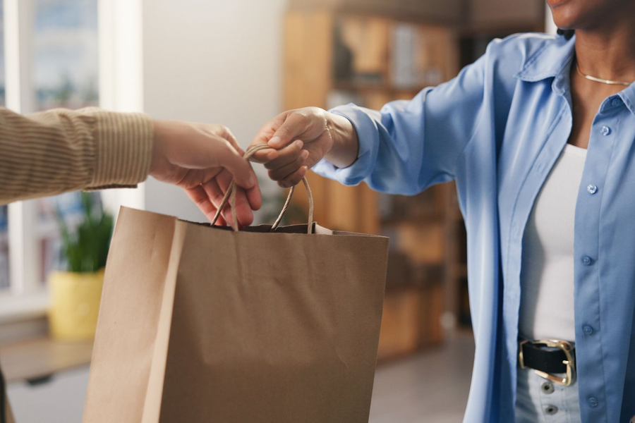 Hands exchanging a brown paper shopping bag in a store setting