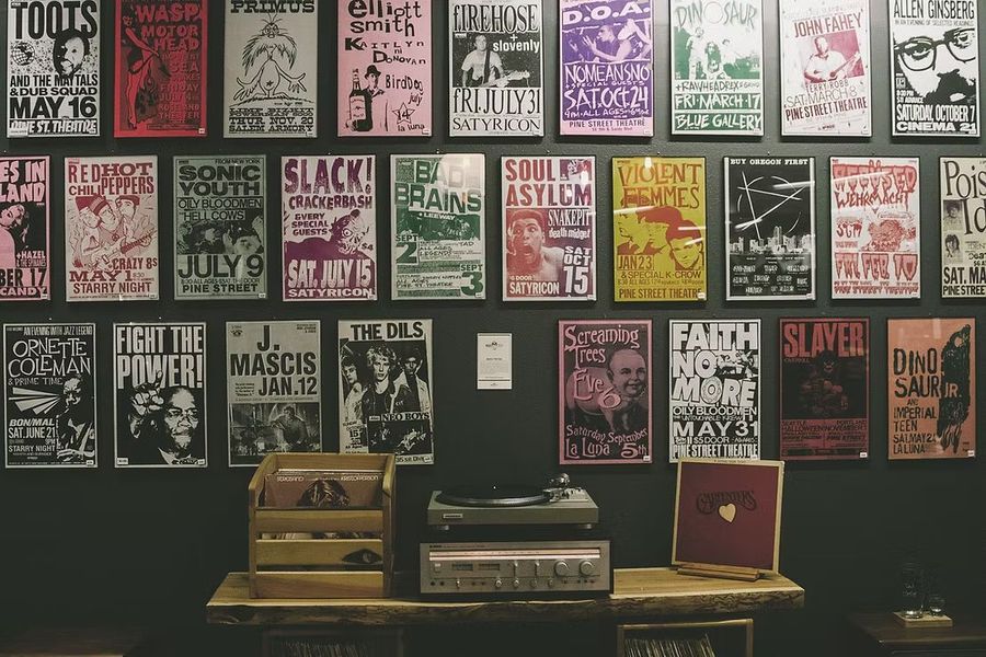 Wall covered with colorful music posters above a table with record players and vinyl albums