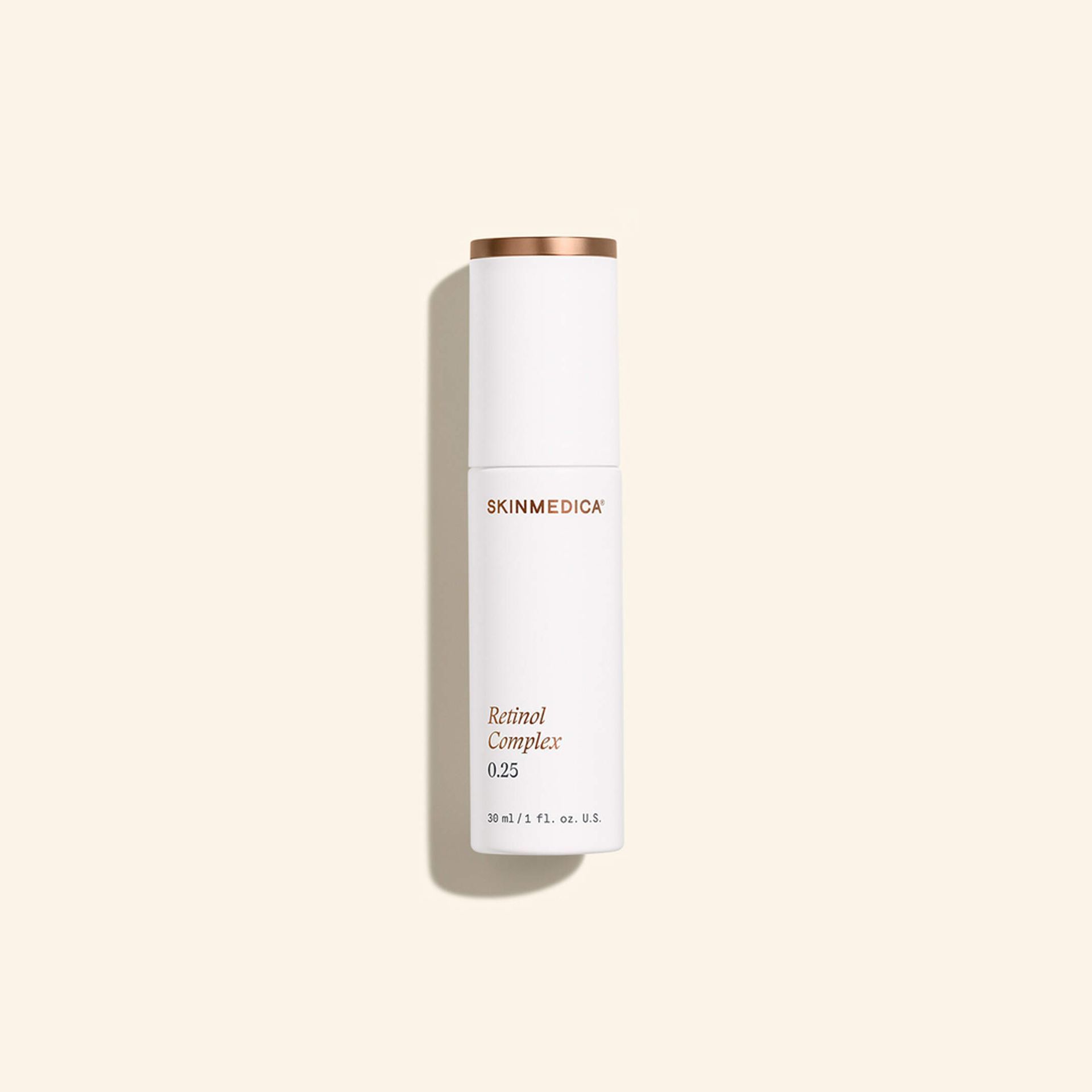 White cylindrical skincare bottle with gold cap on a beige background