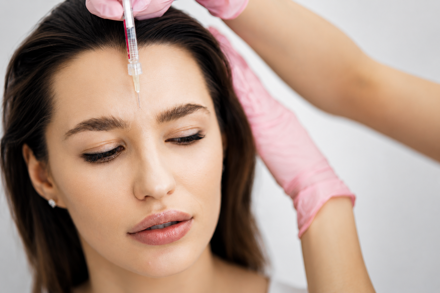 Woman receiving an injection near her forehead while lying down, with gloved hands in view