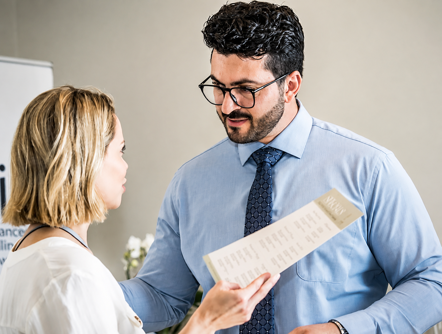 Two people discussing a document in a bright office, one holding papers and gesturing while the other listens.