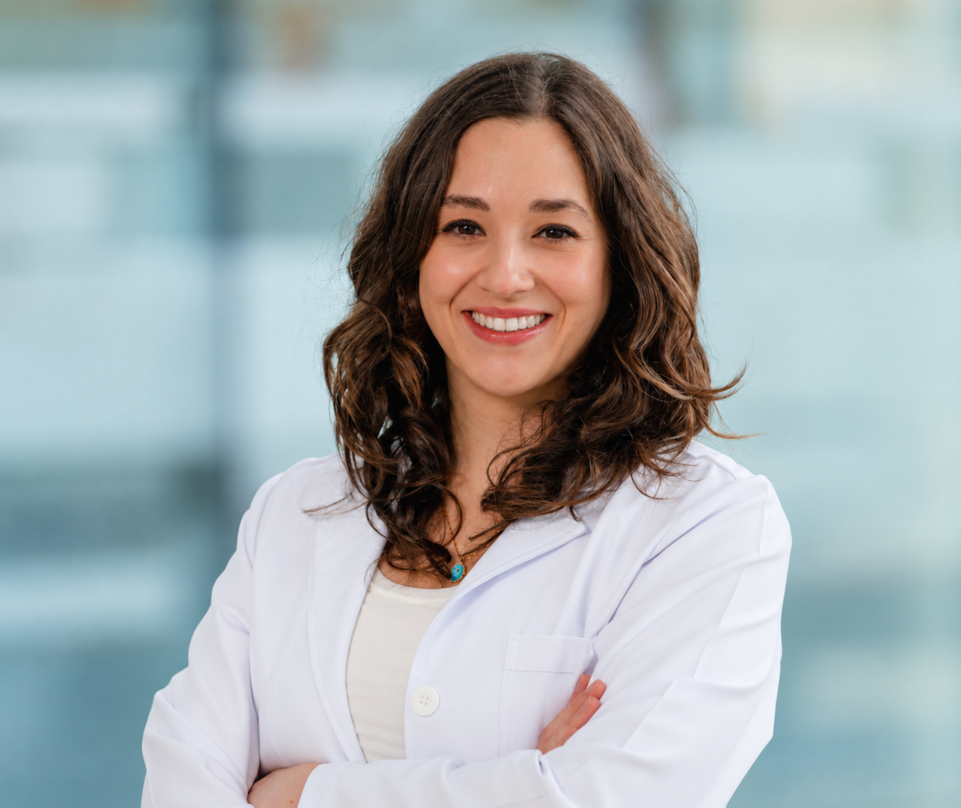 Person in a white lab coat standing with arms crossed against a light background