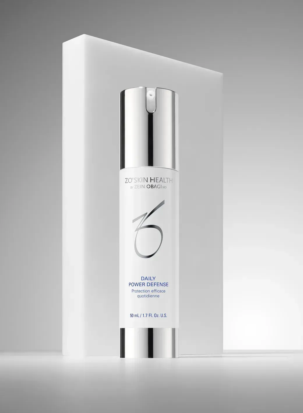 White cosmetic serum bottle with silver cap on a white pedestal against a light gray background