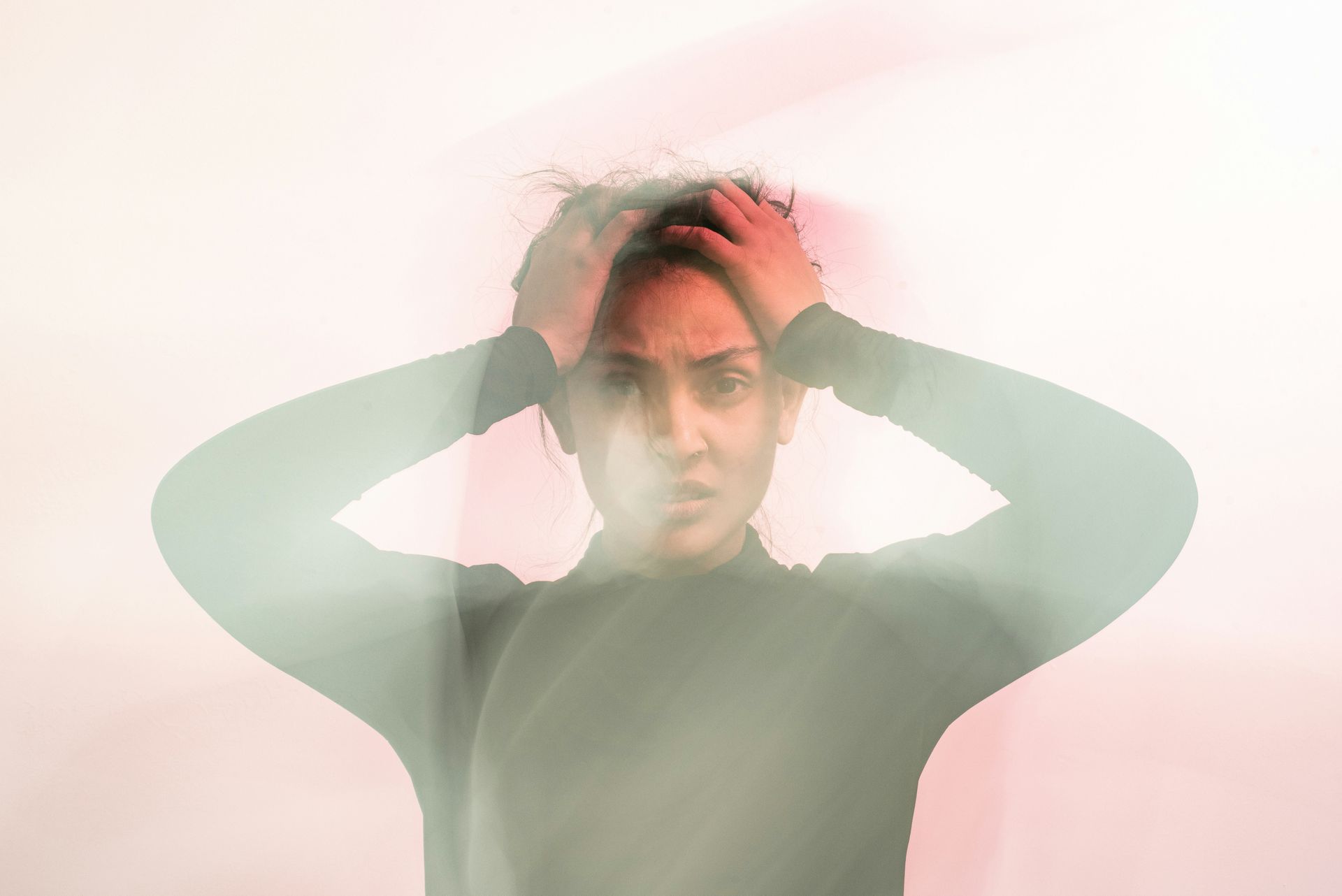Person with hands on head, blurred motion effect. Appears distressed, looking at camera.