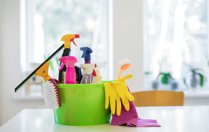 A green bucket filled with cleaning supplies is sitting on a table.