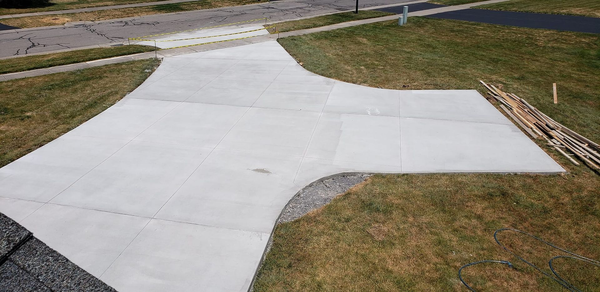 Concrete driveway curving from street, expanding into a wider pad, surrounded by grass.