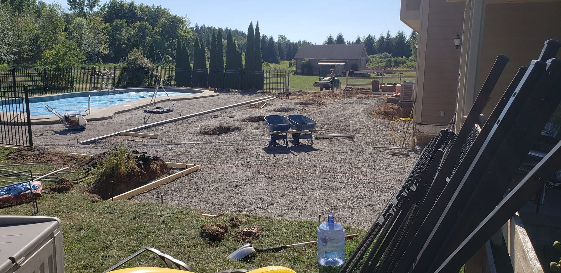 Backyard landscaping in progress, gravel bed surrounding a pool. Clear skies, trees, and a house in the distance.