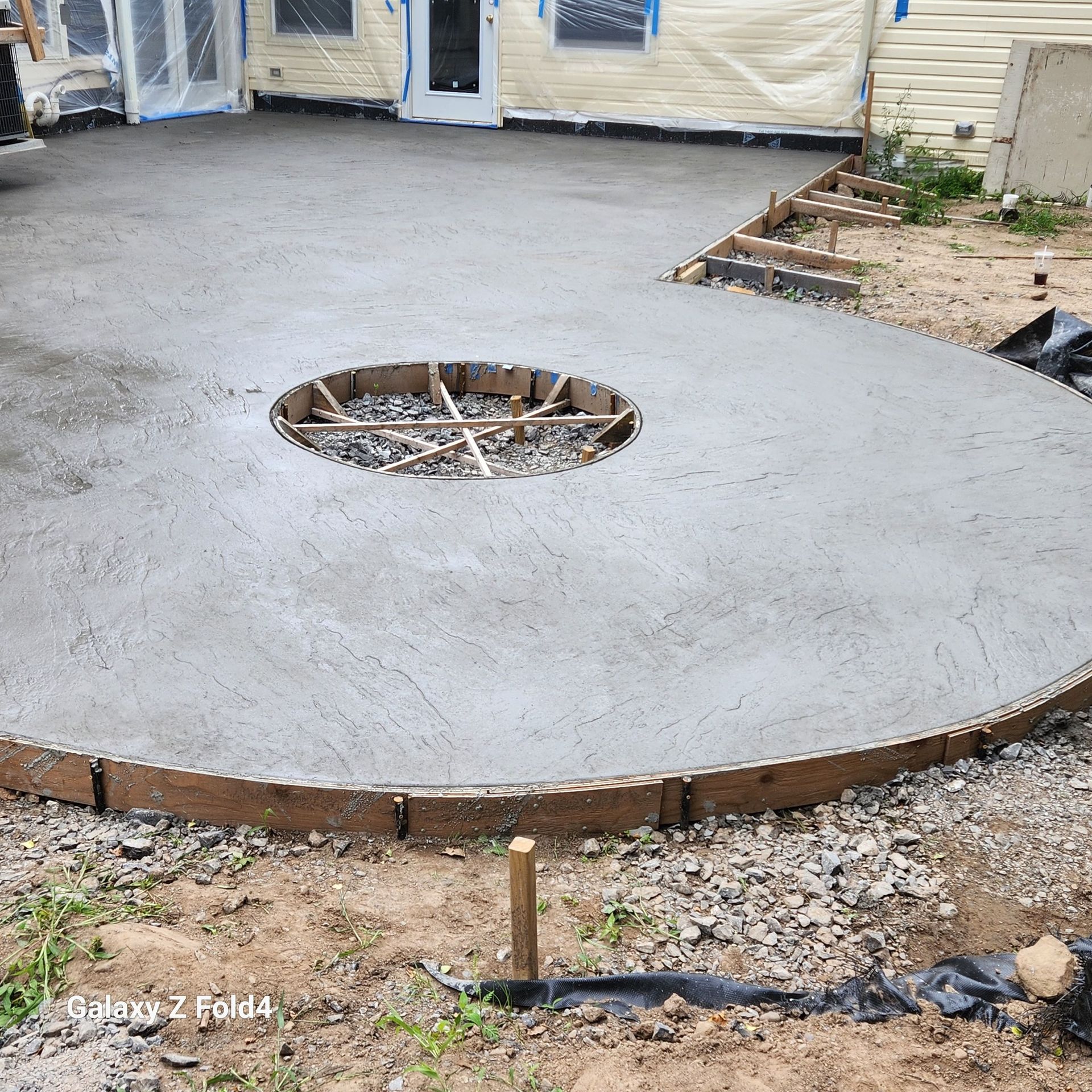 Freshly poured concrete patio with a circular cutout, wooden formwork, and the house in the background.