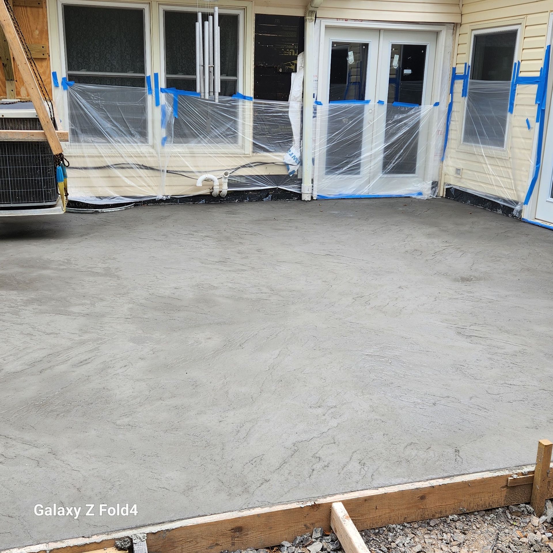 A freshly poured concrete patio next to a house with windows and a door.