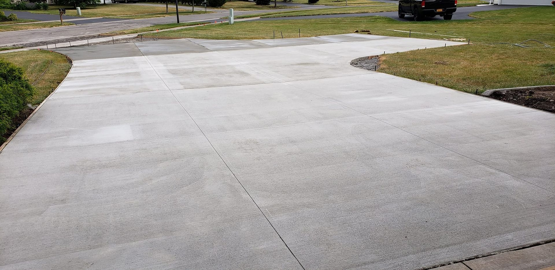 Concrete driveway with a car parked at the end, grassy areas on either side, sunny day.