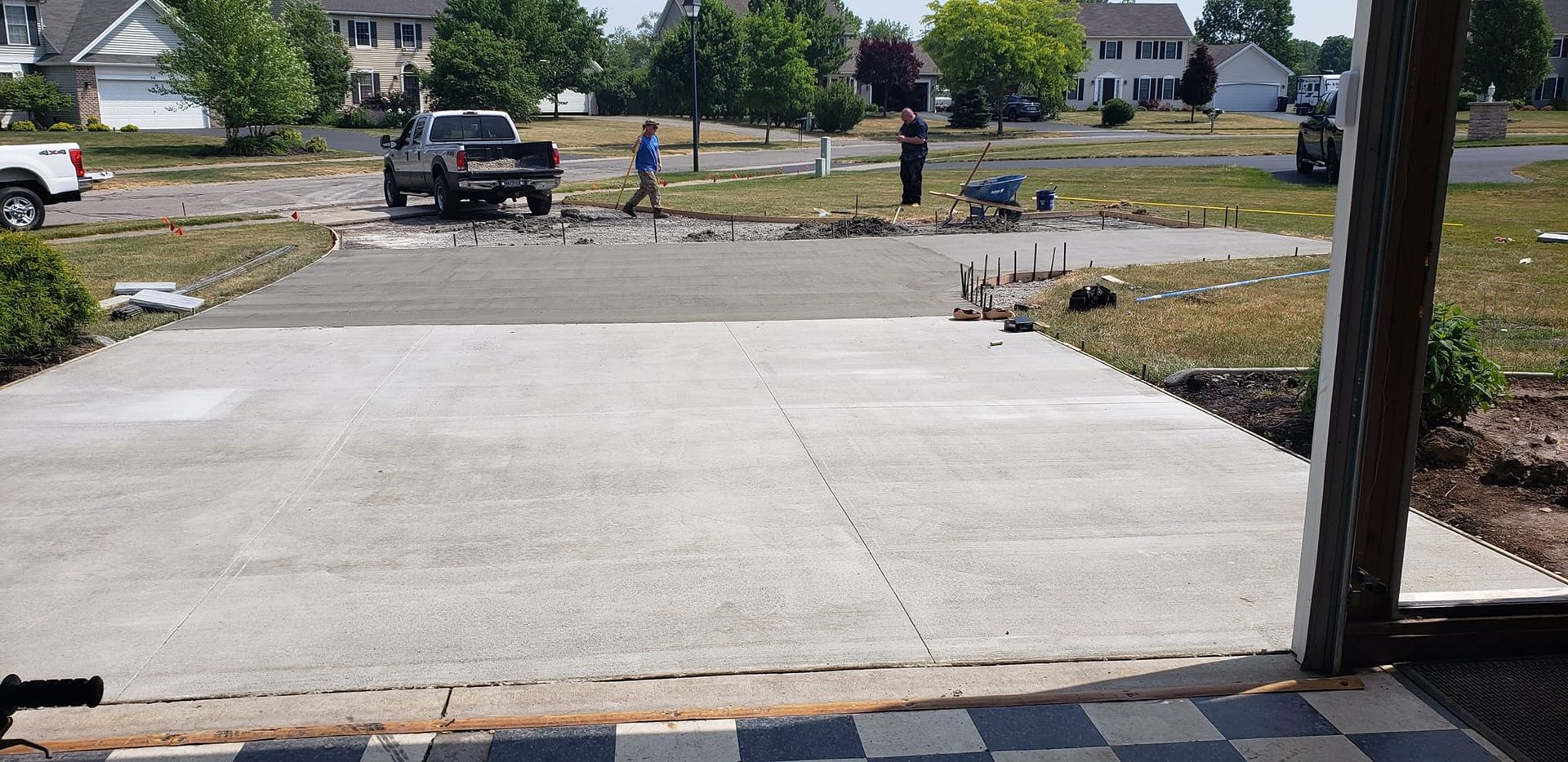 Workers pouring concrete driveway in suburban setting.