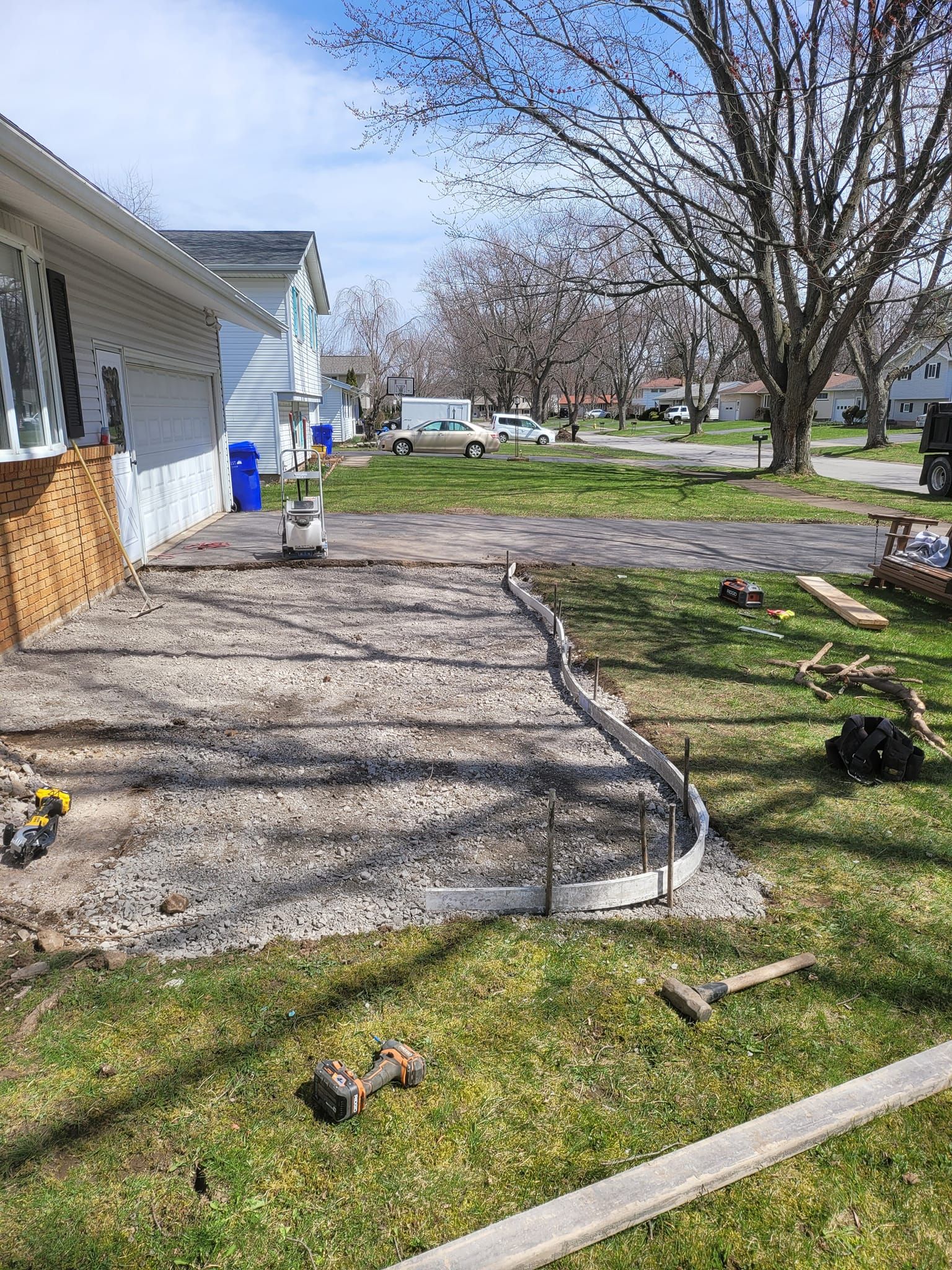 Concrete patio construction in progress; gray concrete base with curved formwork, tools on grass lawn.