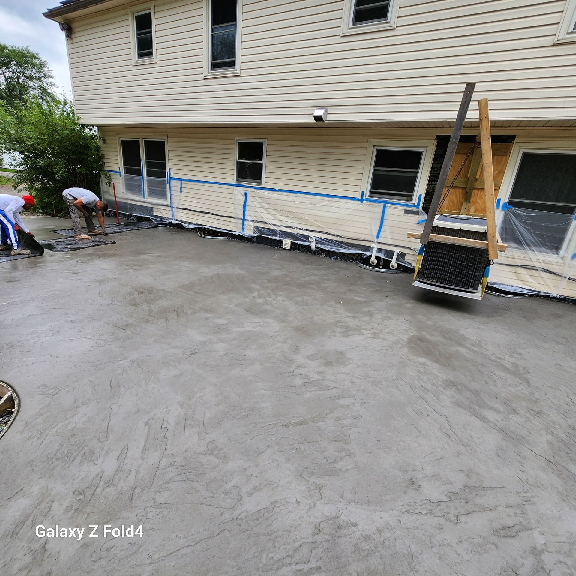 Workers pouring concrete patio next to a light-colored house. Blue tape protects the siding.