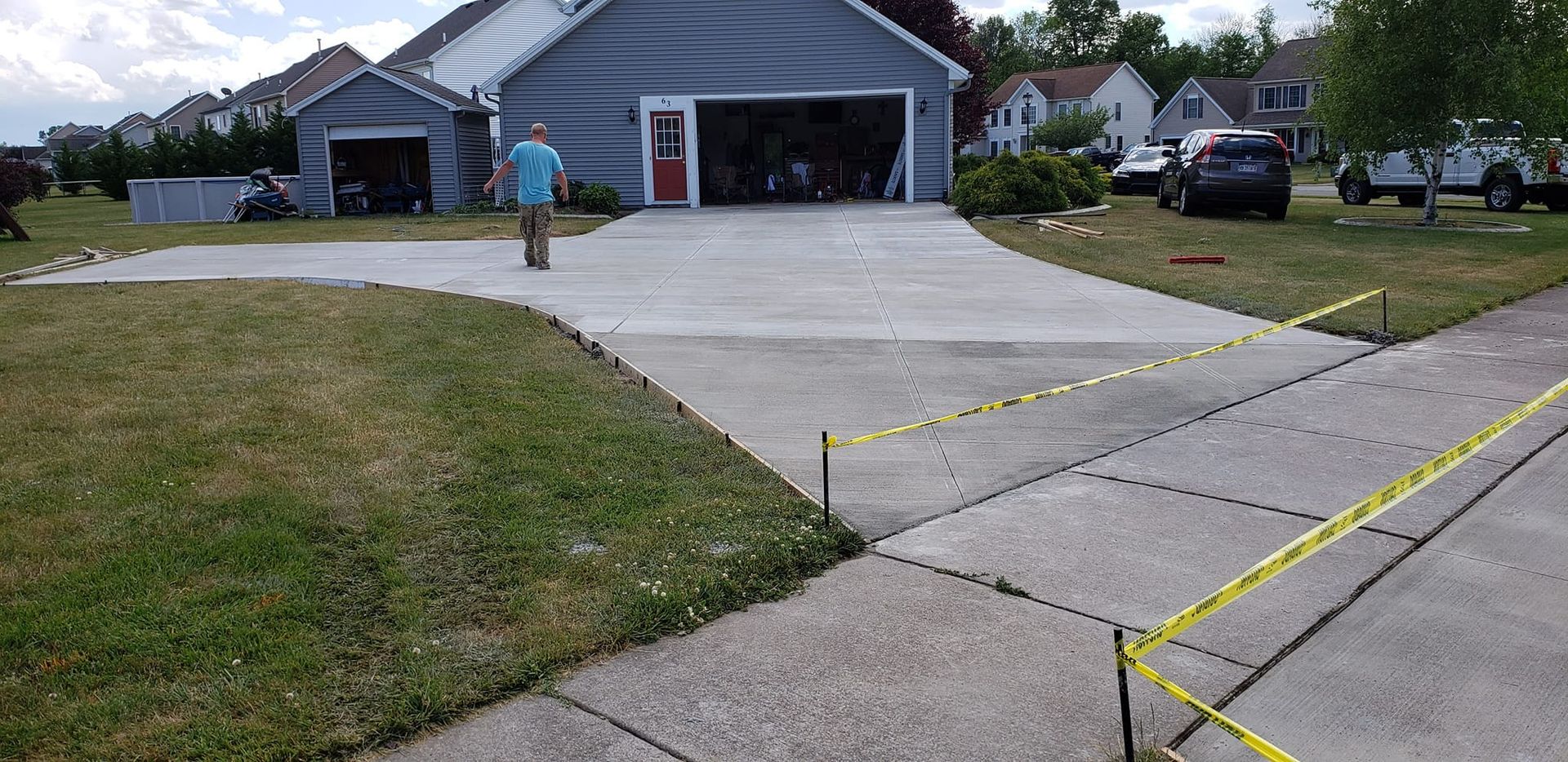 Driveway with house and garage, person walking on concrete; yellow caution tape present.