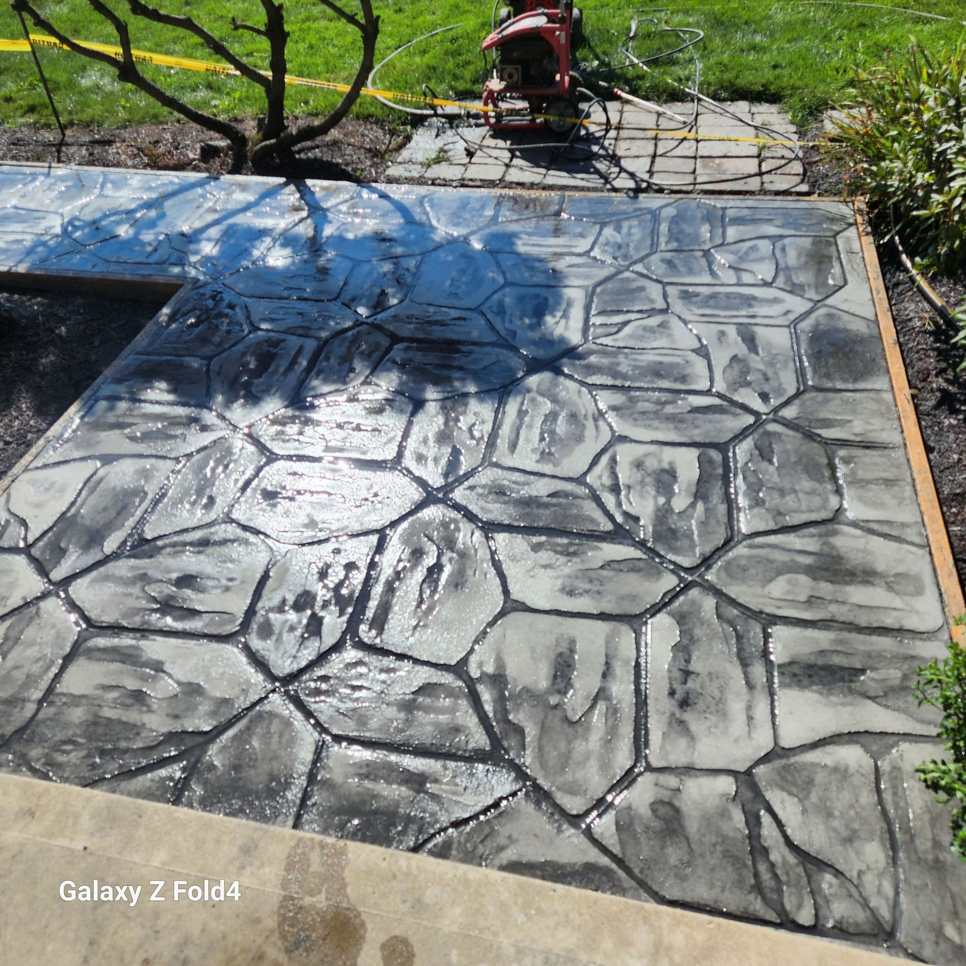 Newly installed, stamped concrete patio with stone-like pattern; wet with sheen.