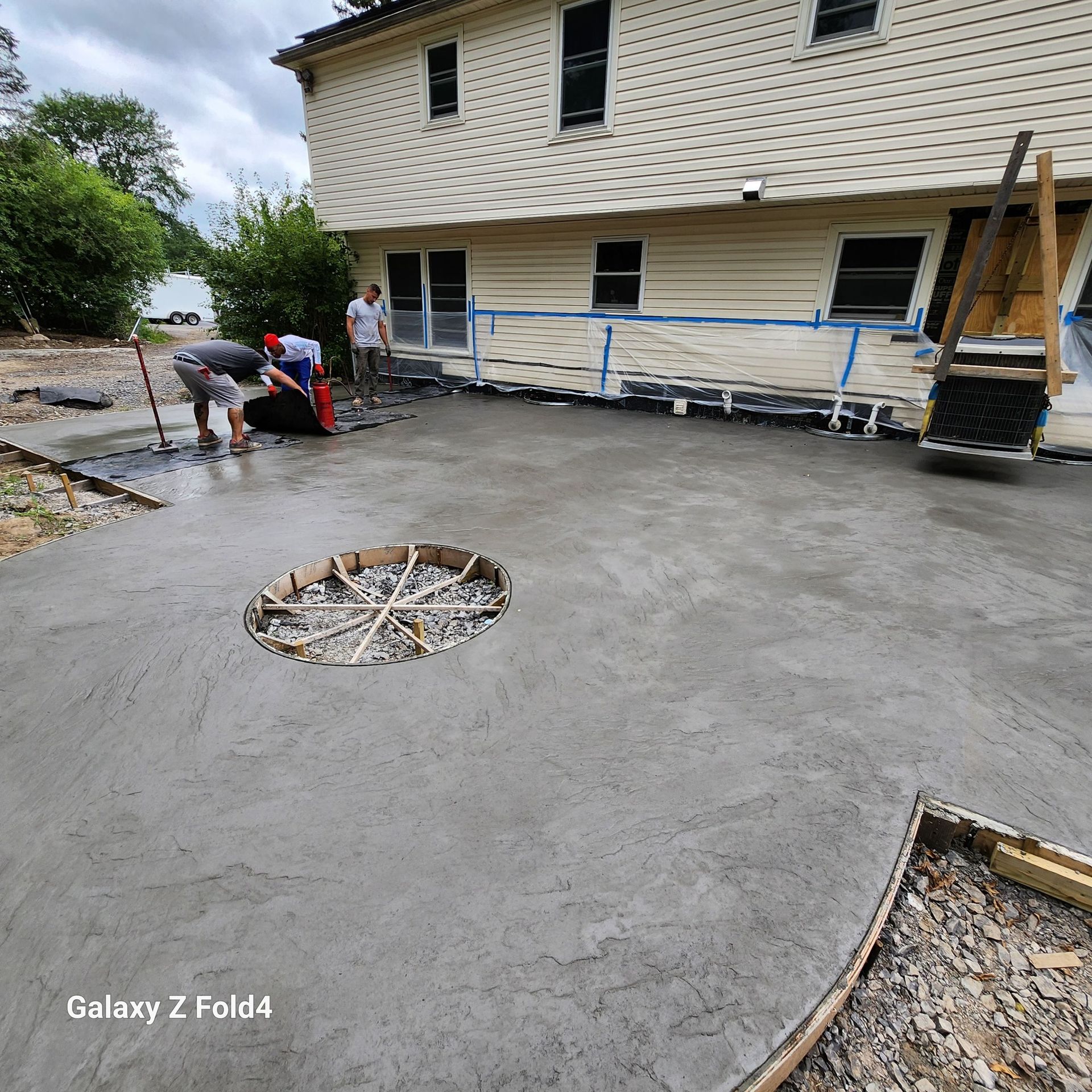 Workers pouring concrete driveway next to a house with a large hole.