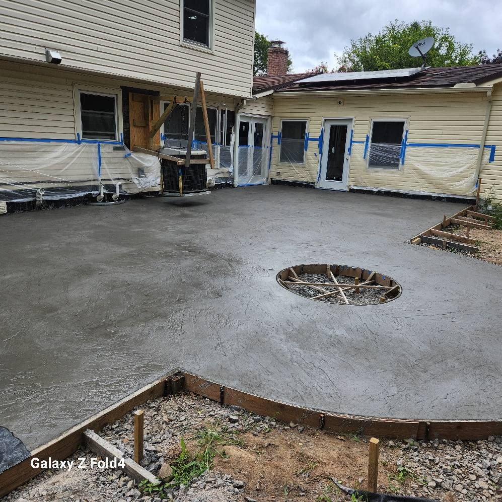Newly poured concrete patio, surrounded by a house, with a circular fire pit area in the center.