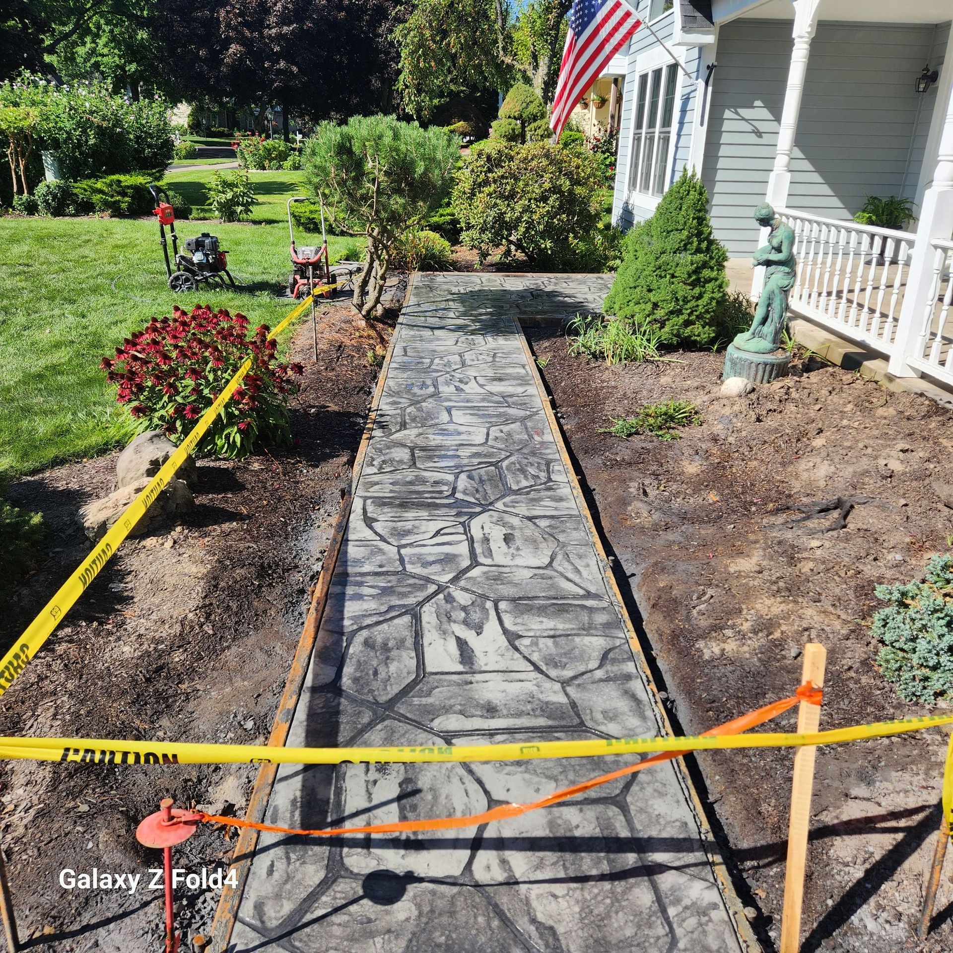 Stamped concrete walkway under construction; caution tape, yard, and house.