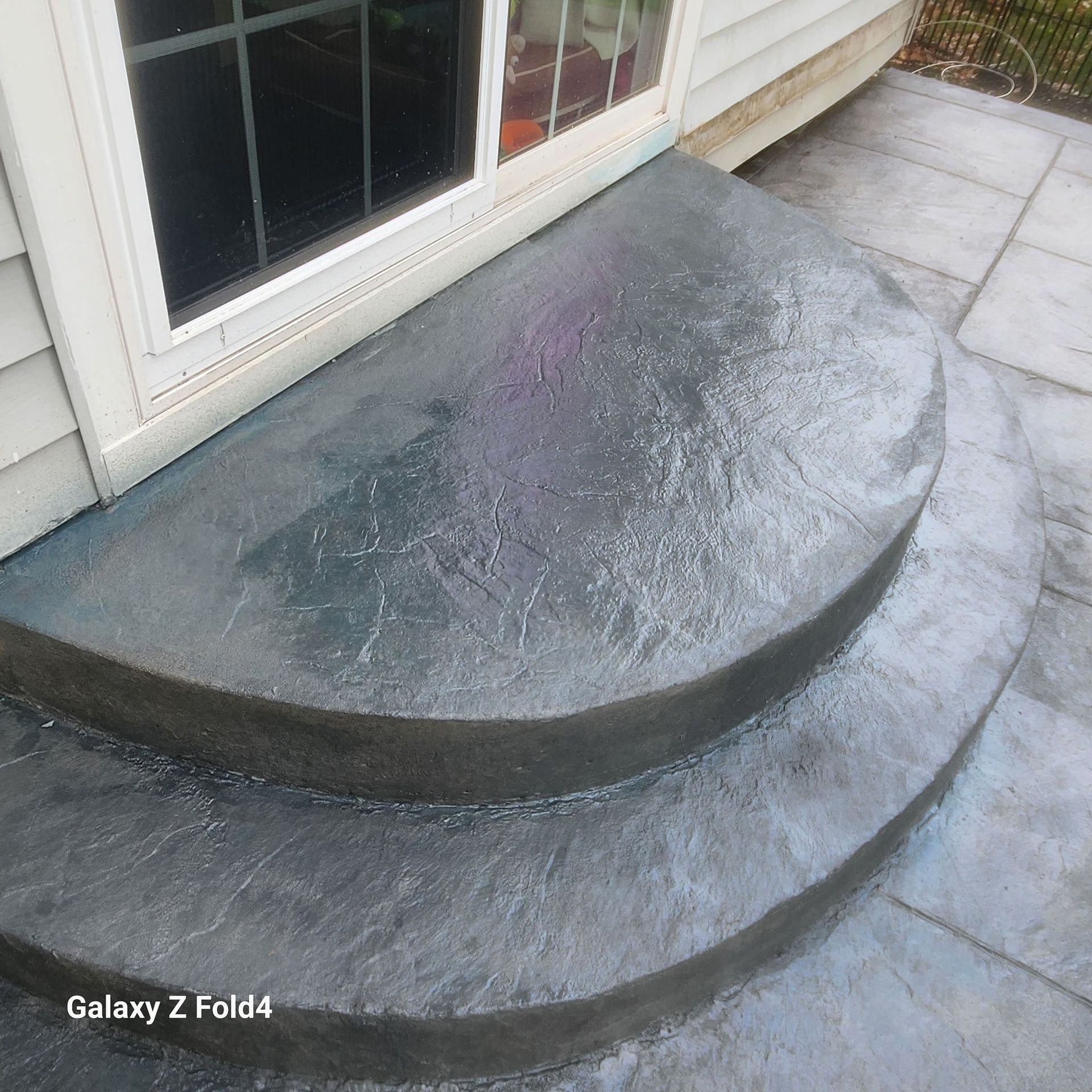 Concrete steps leading to a sliding glass door. The steps are semi-circular and grey.