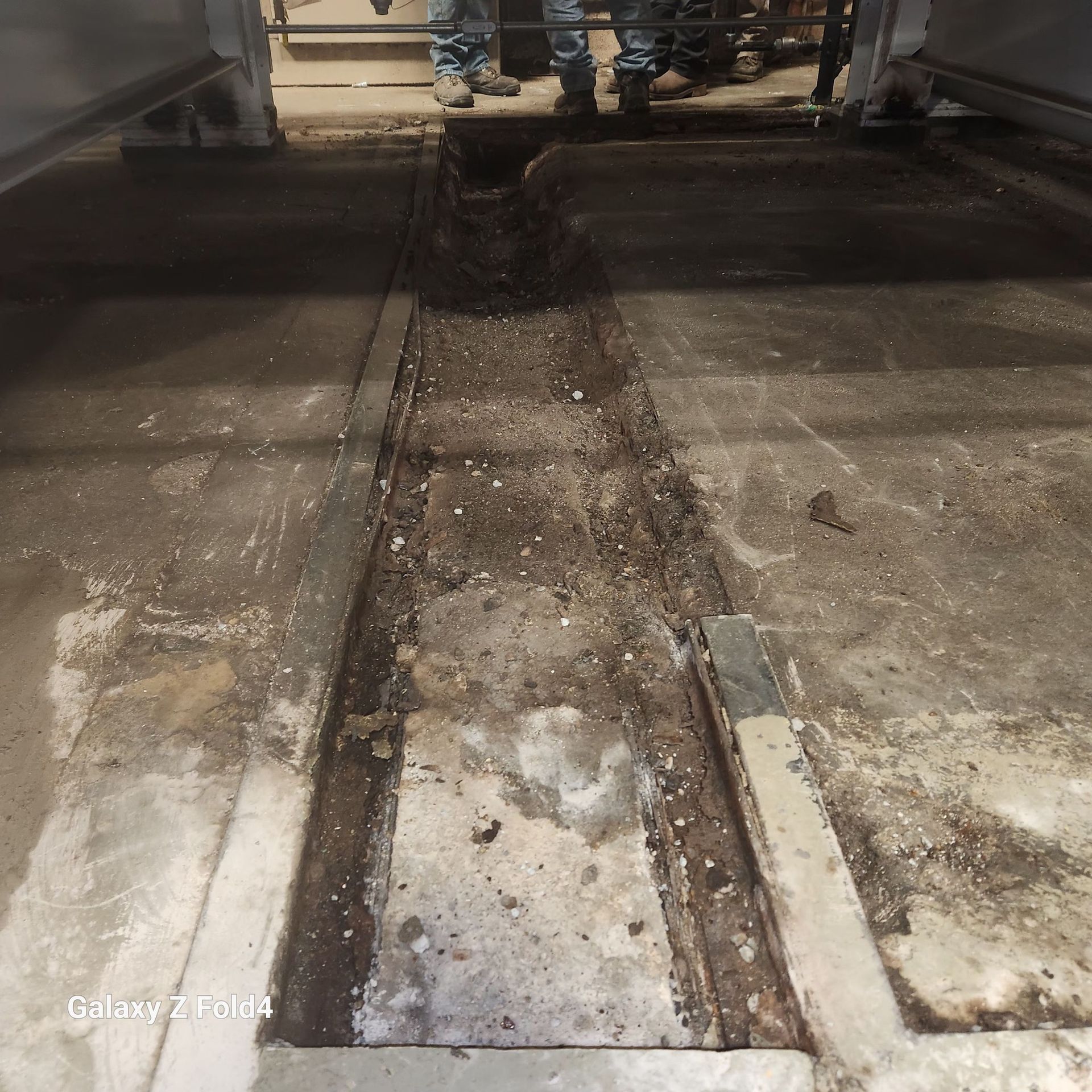 Dirty industrial floor with a long narrow trench. People standing in background.