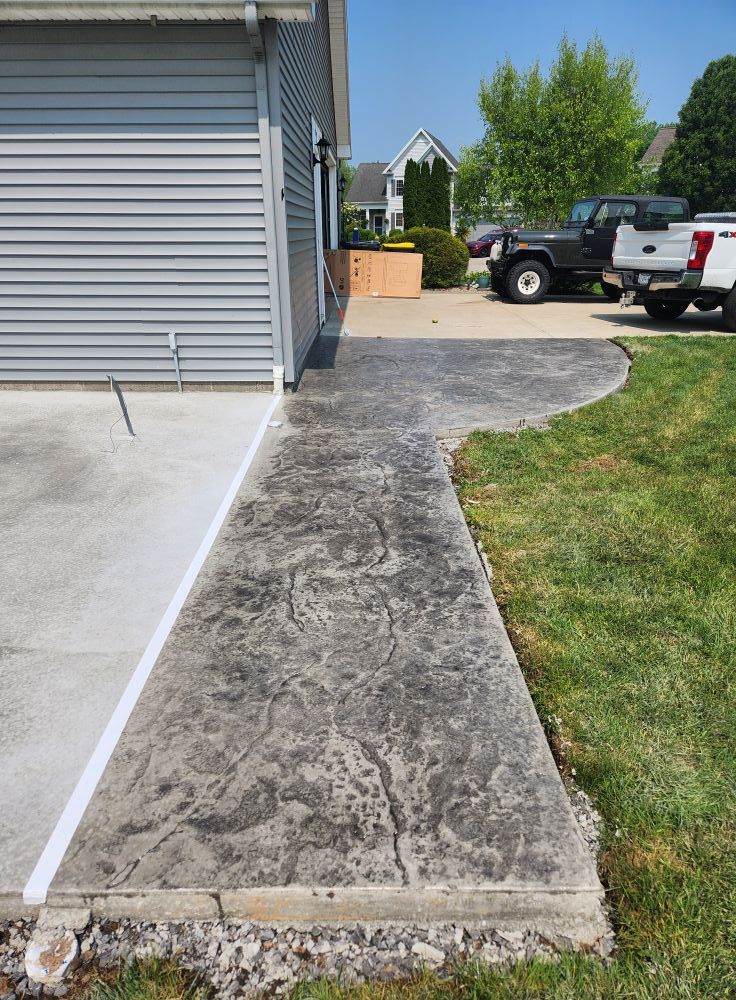 Concrete sidewalk next to garage with stamped stone texture and grass lawn.