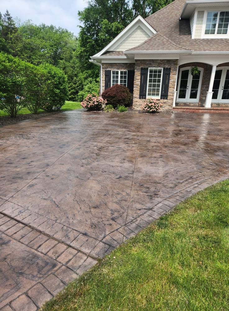 Brown stamped concrete driveway with brick border in front of a house.