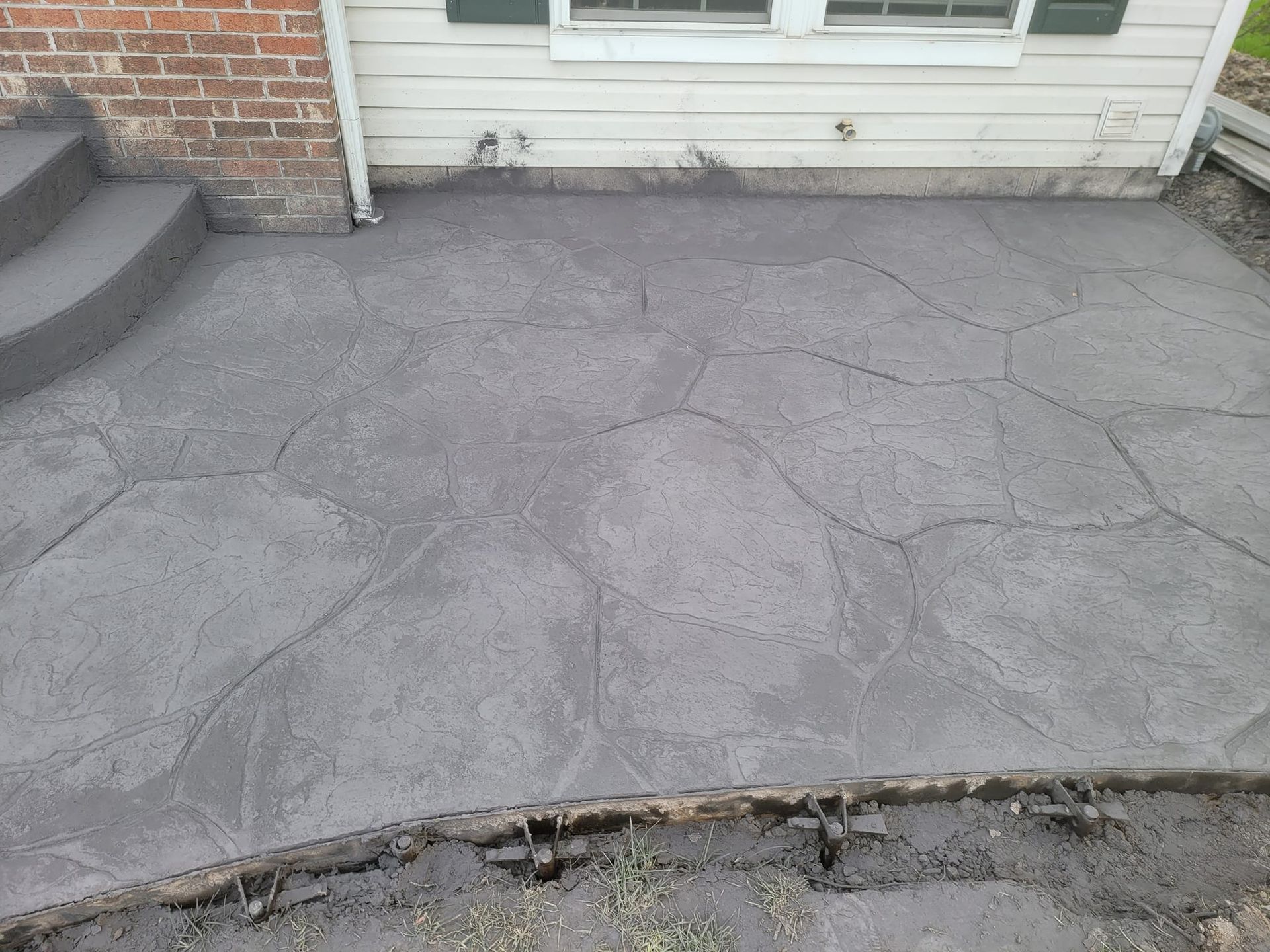 Gray, stamped concrete patio with stone pattern, brick steps, and house siding.