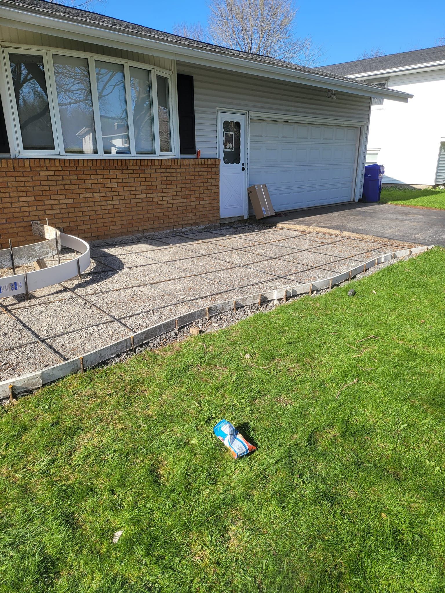 House with concrete patio under construction, bordered by grass and stone.