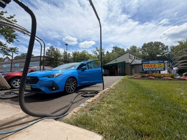 Bright blue SUV at a car wash with hose in foreground and a “Great prices” sign outside the building