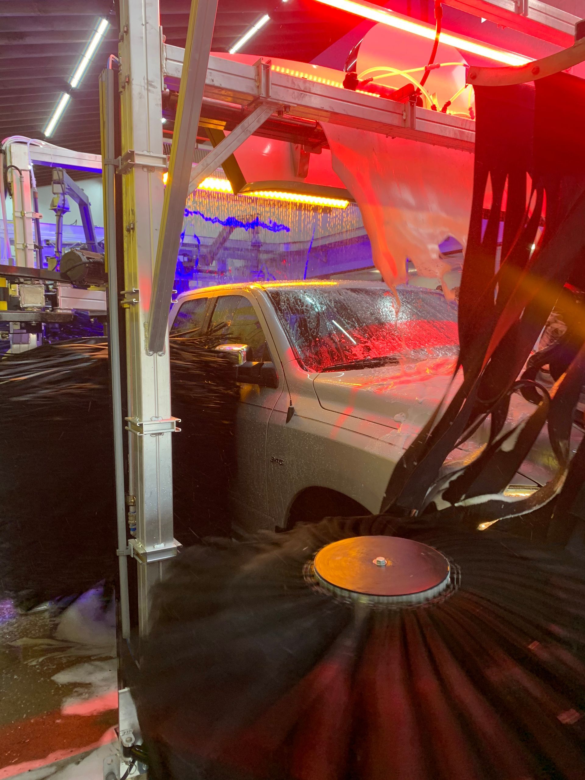 Car in an automated car wash, splashed with soap and lit by red and blue neon lights