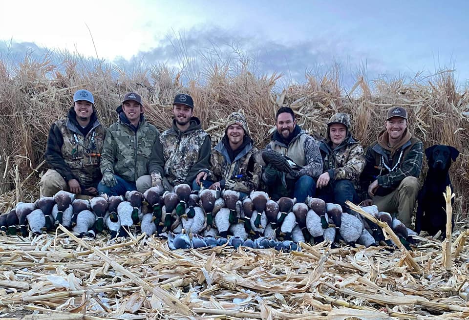 A group of people are posing for a picture goose hunting in a field of corn.