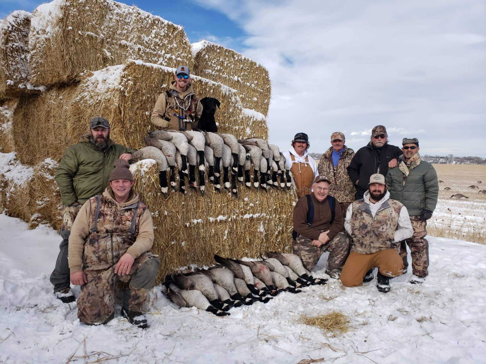 A group of men are posing for a picture in front of bales of hay.