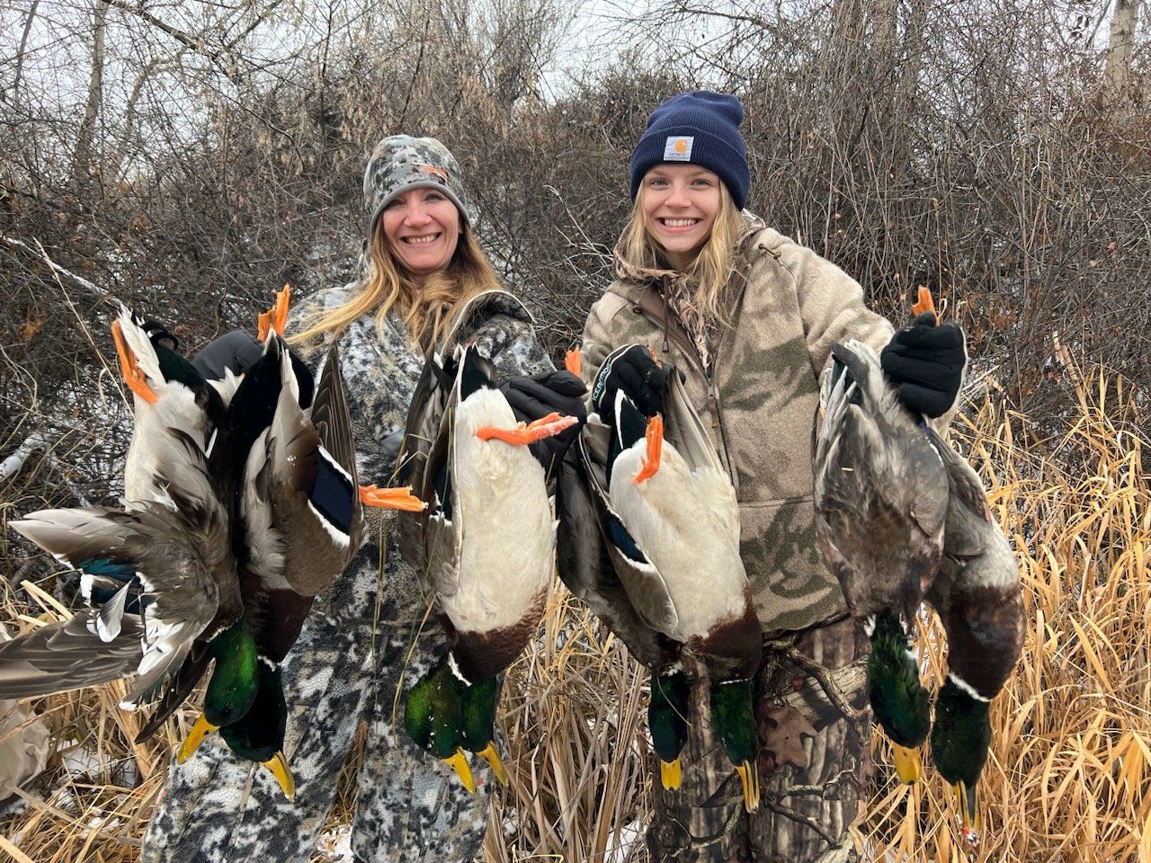 Two women are holding ducks in their hands in a field.