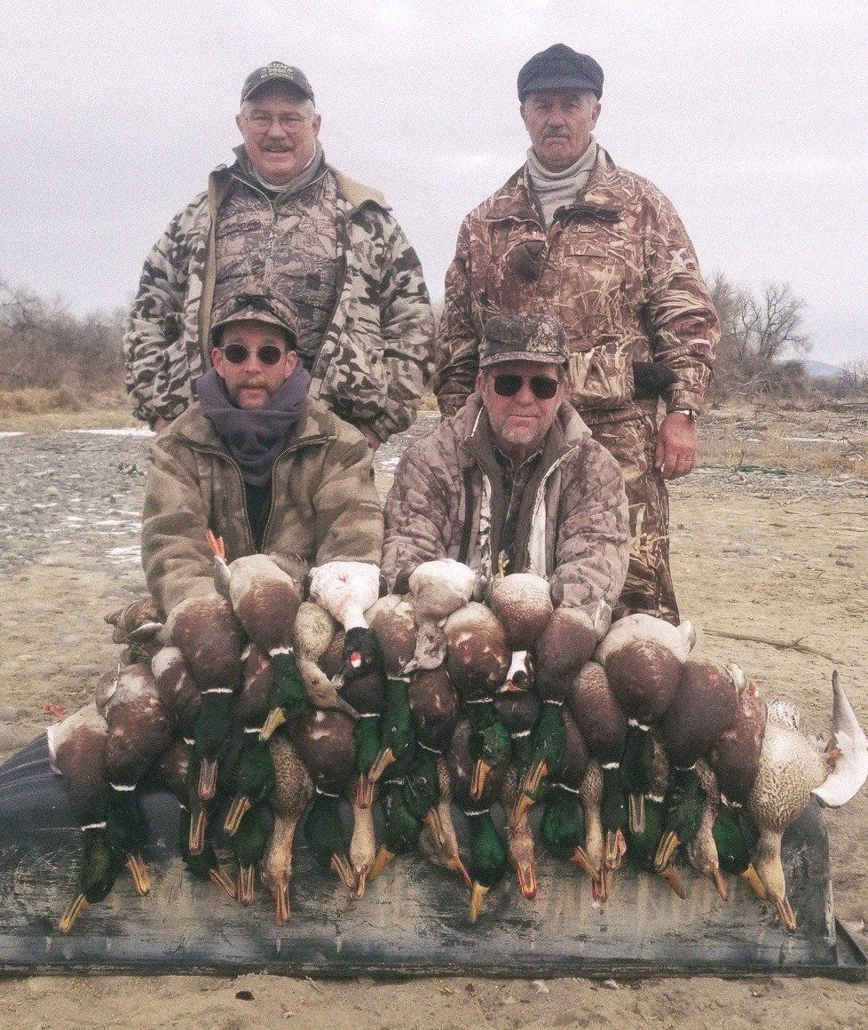 A group of men standing next to a pile of ducks