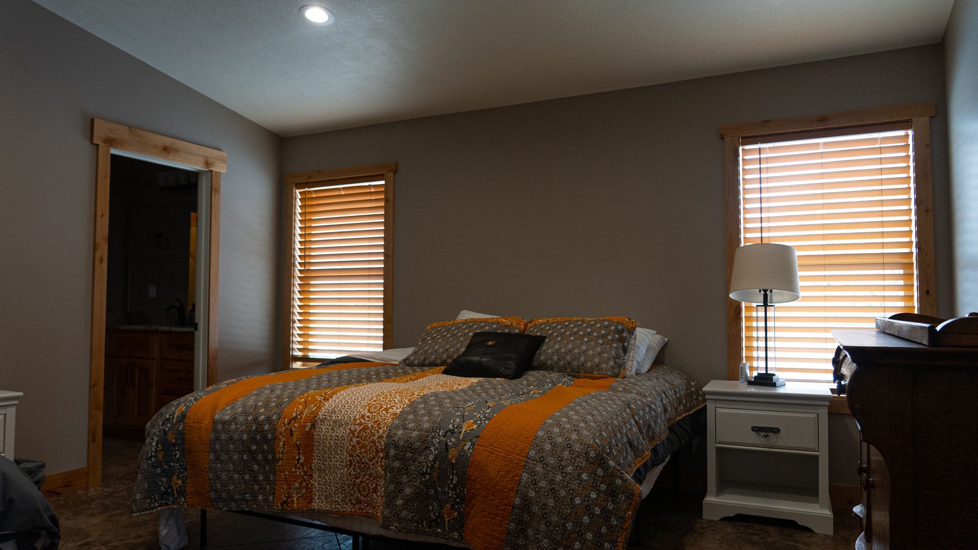 A bedroom with a bed , nightstand , lamp and two windows.