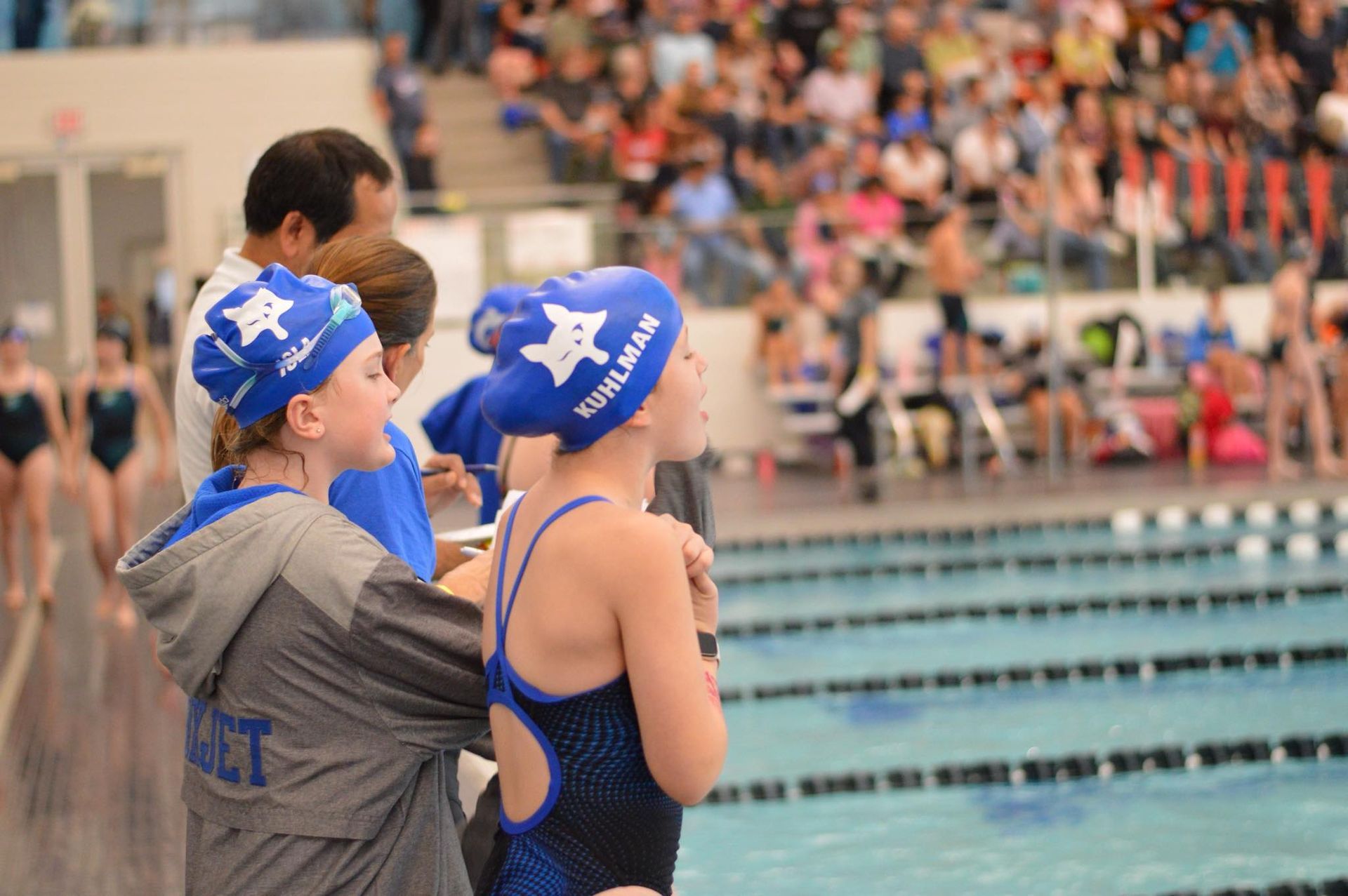 Swimmers with Foxjets Swim caps on, cheer on other swimmers at a swim meet