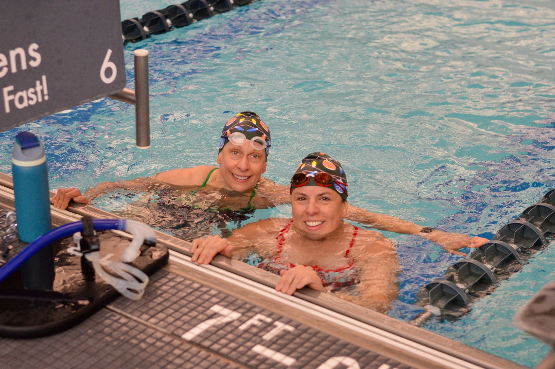 2 masters swimmers smile in the pool while holding onto the swimming pool wall
