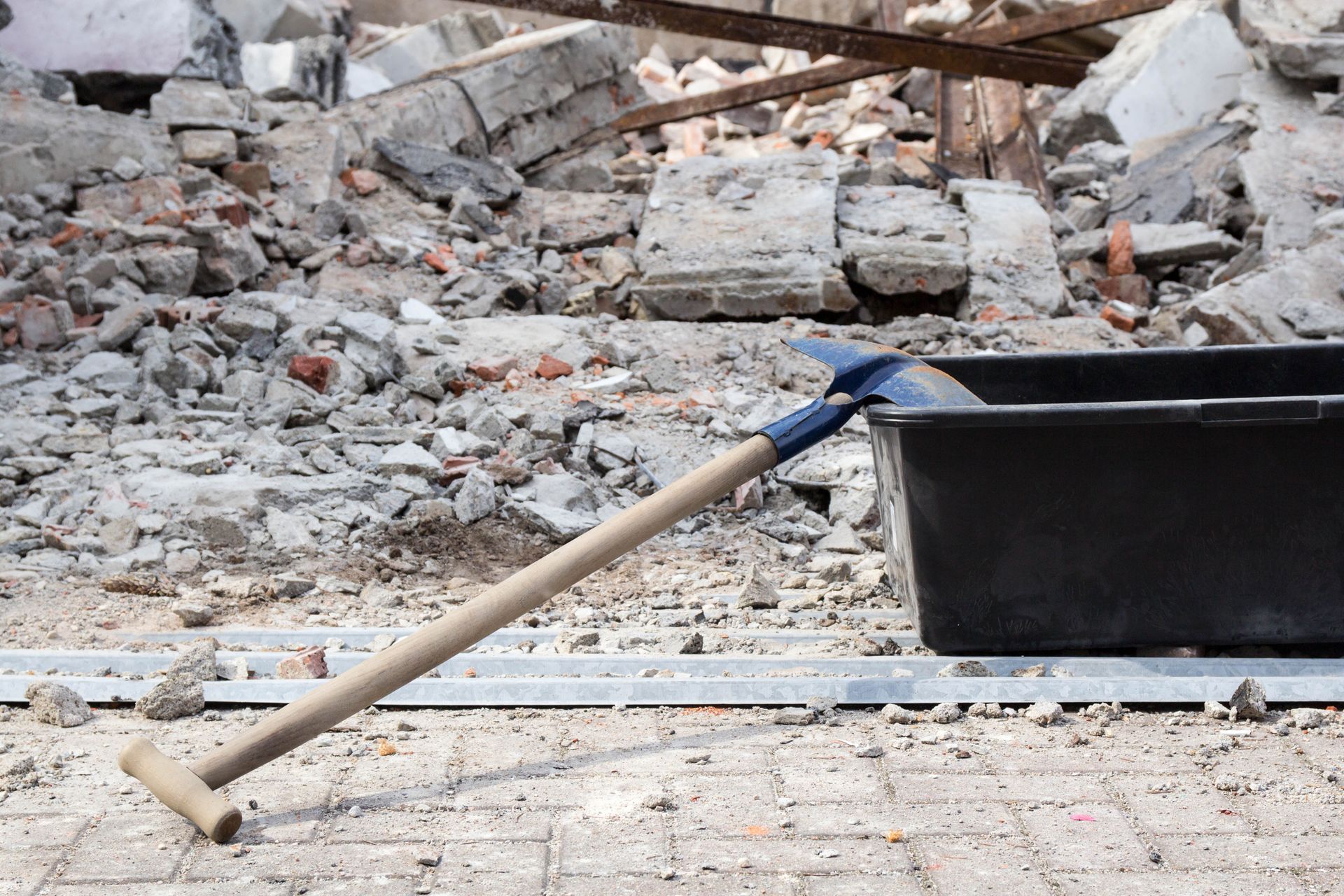 A shovel is laying on the ground next to a black bucket.