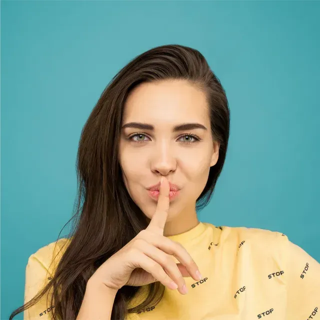 A woman in a yellow shirt is holding her finger to her lips.