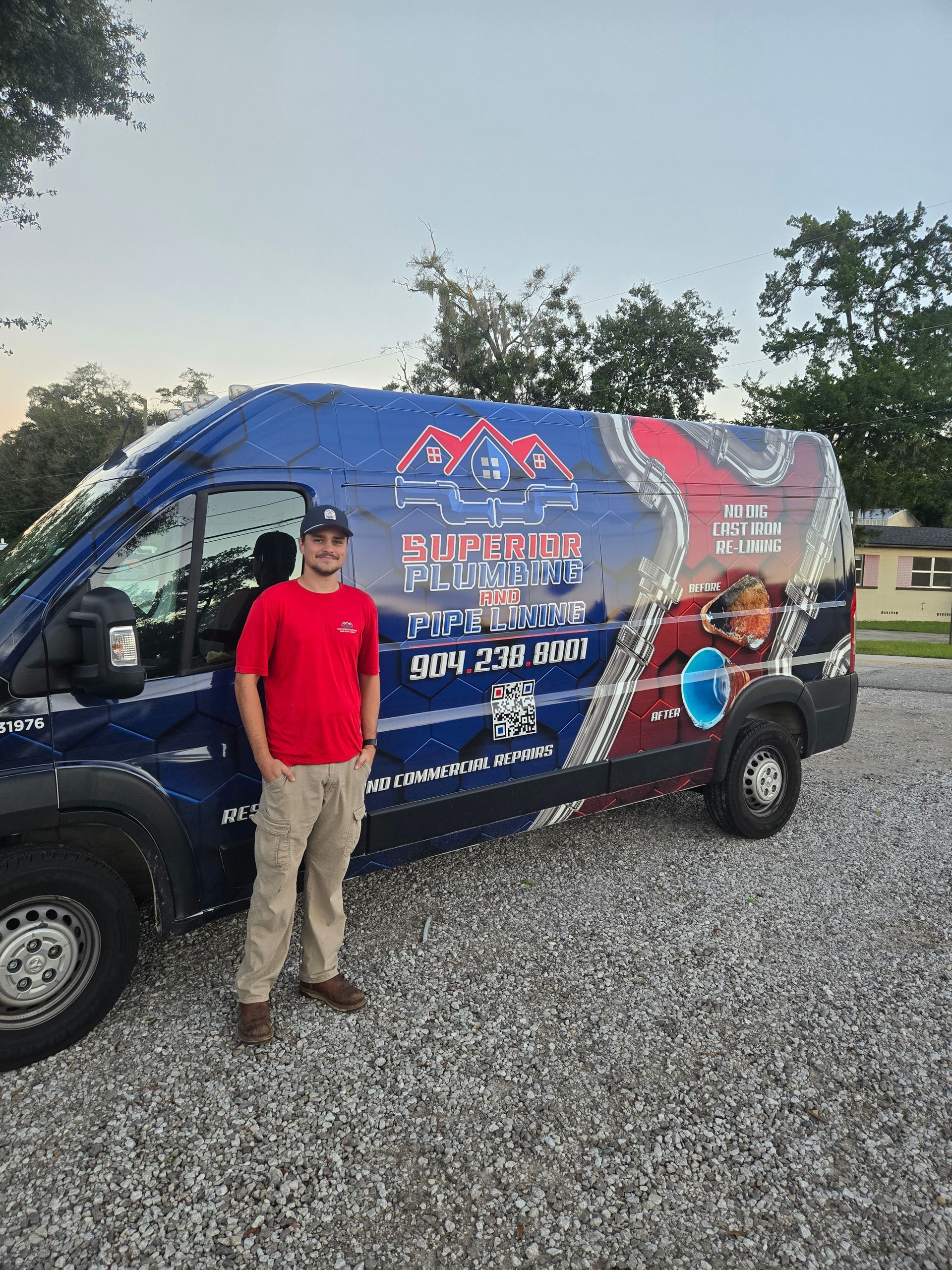 A person in a red shirt stands next to a blue, branded cargo van with a mountain logo in a gravel lot.