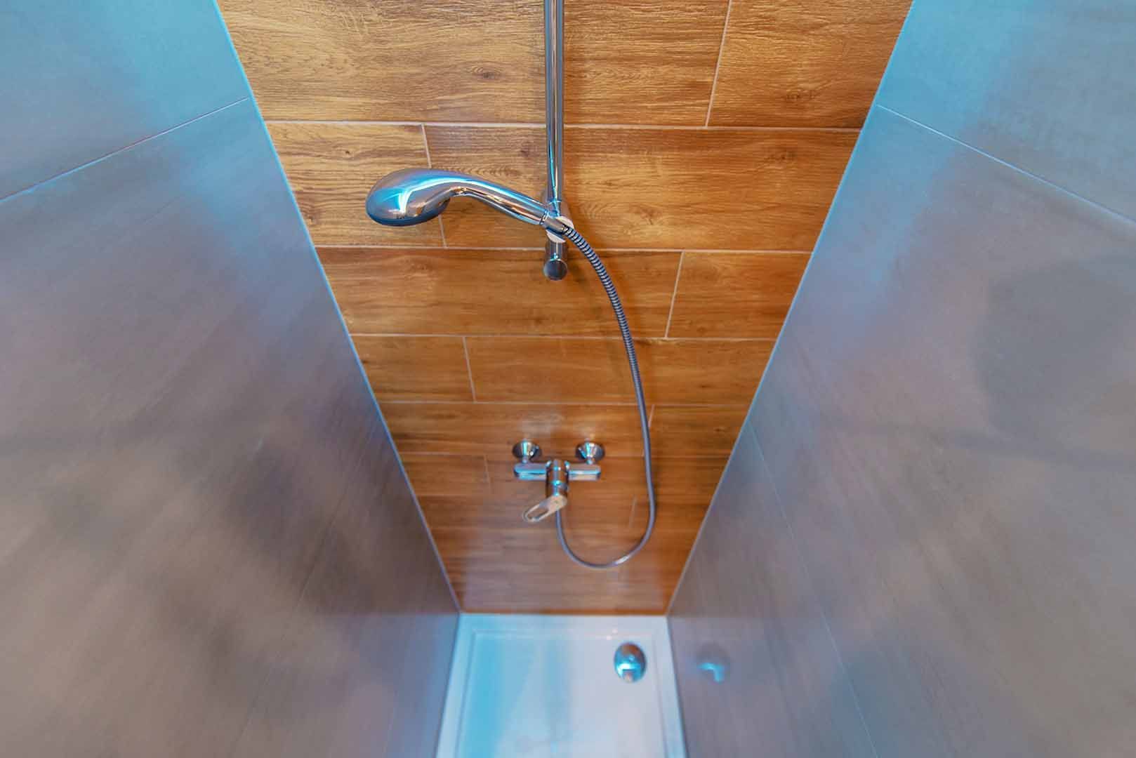 A shower stall with wood-look tile on the back wall, a stainless steel shower fixture, and grey side walls.