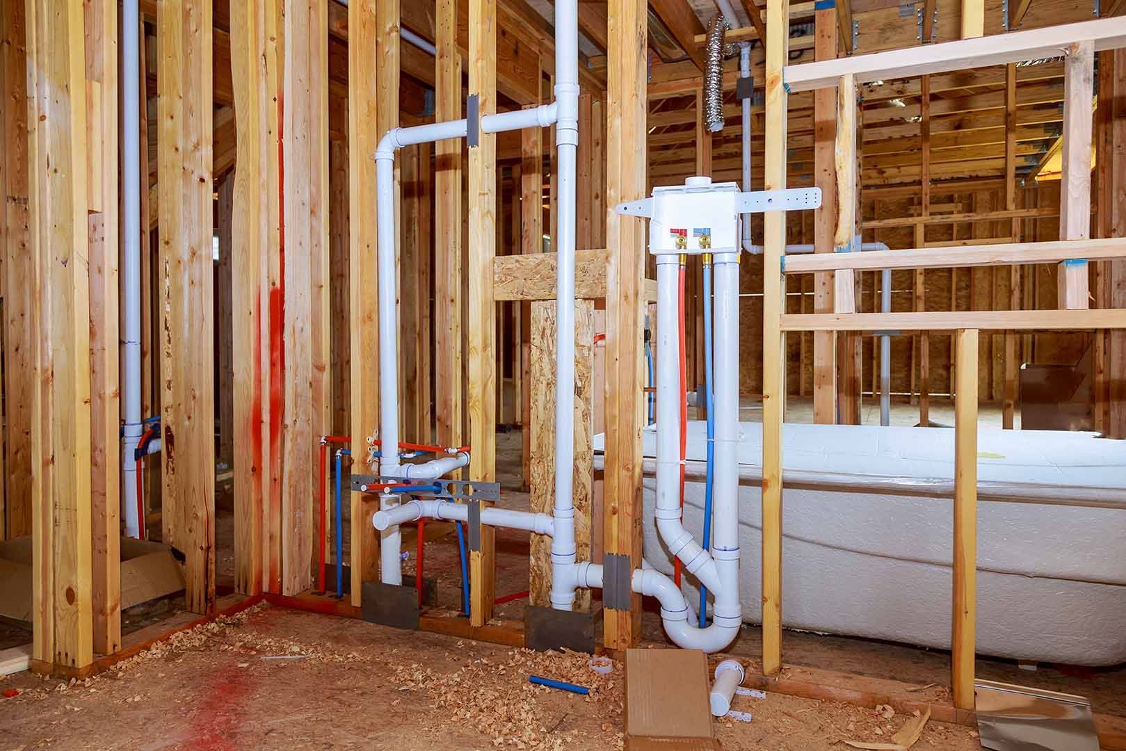 Construction framing for a bathroom featuring white PVC plumbing pipes and red and blue PEX water lines.