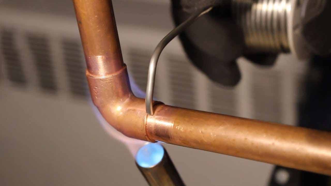 A propane torch heats a copper pipe fitting while a wire of solder is applied to the joint to create a seal.