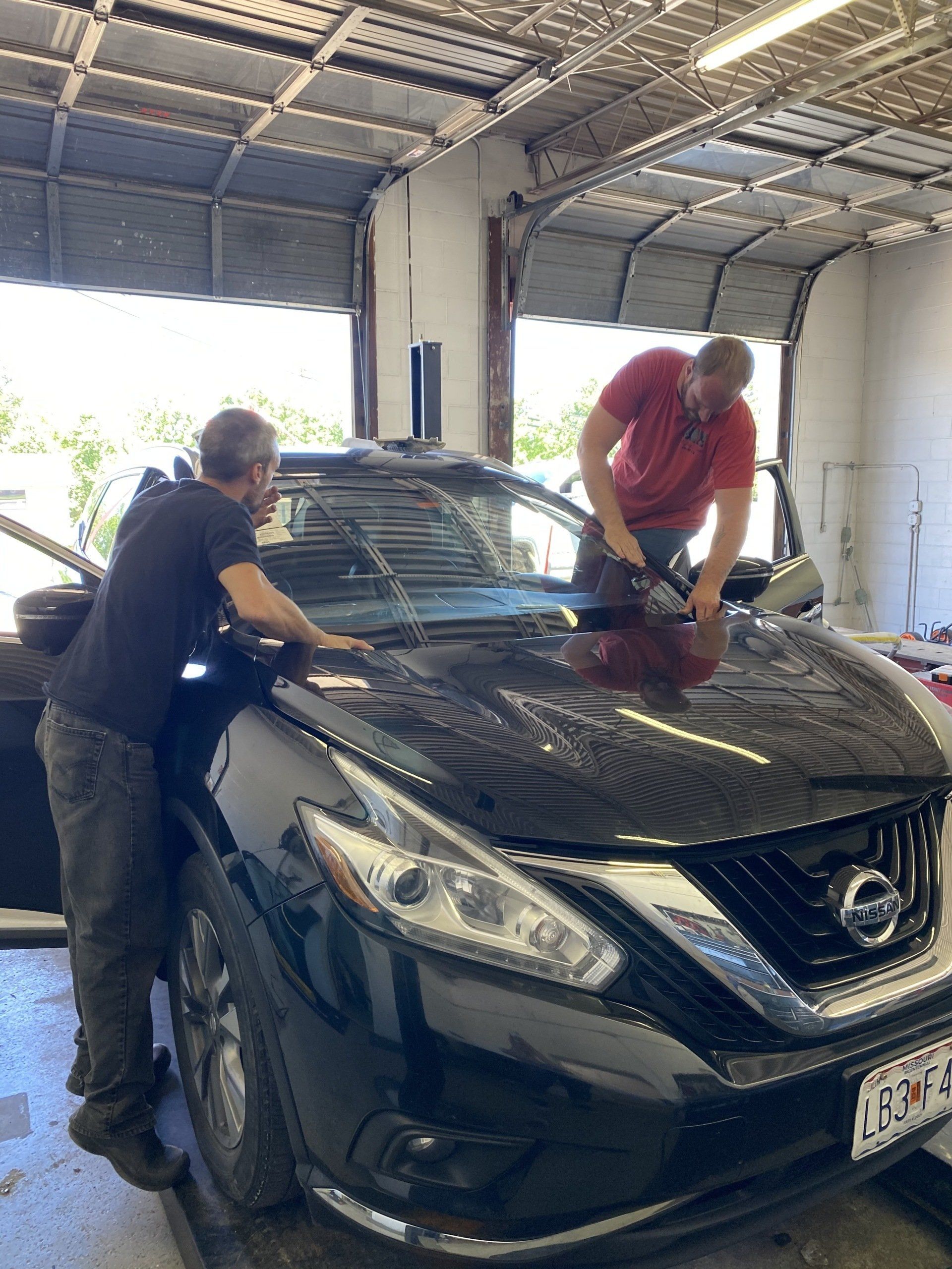 Two people cleaning a black Nissan SUV inside a garage.
