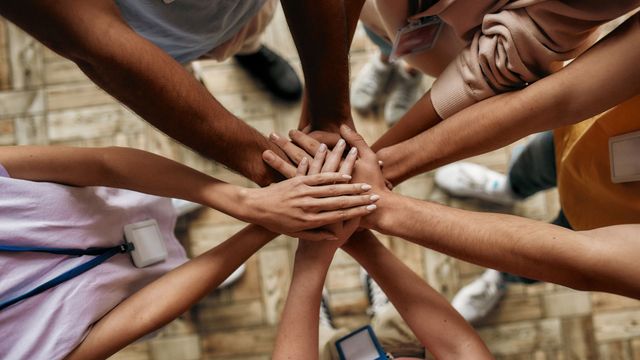 Several hands stacked together in a team huddle on a stone floor