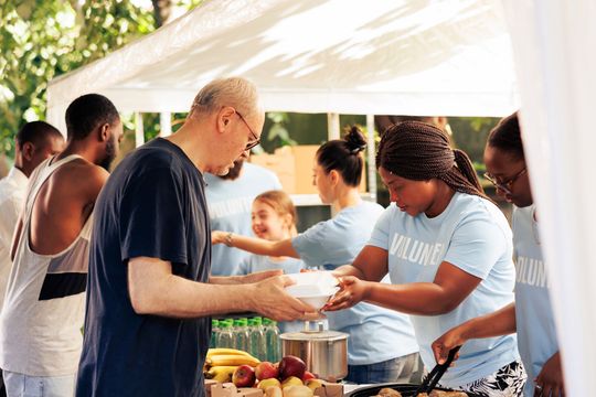 Volunteers serving food at an outdoor community event under a white tent