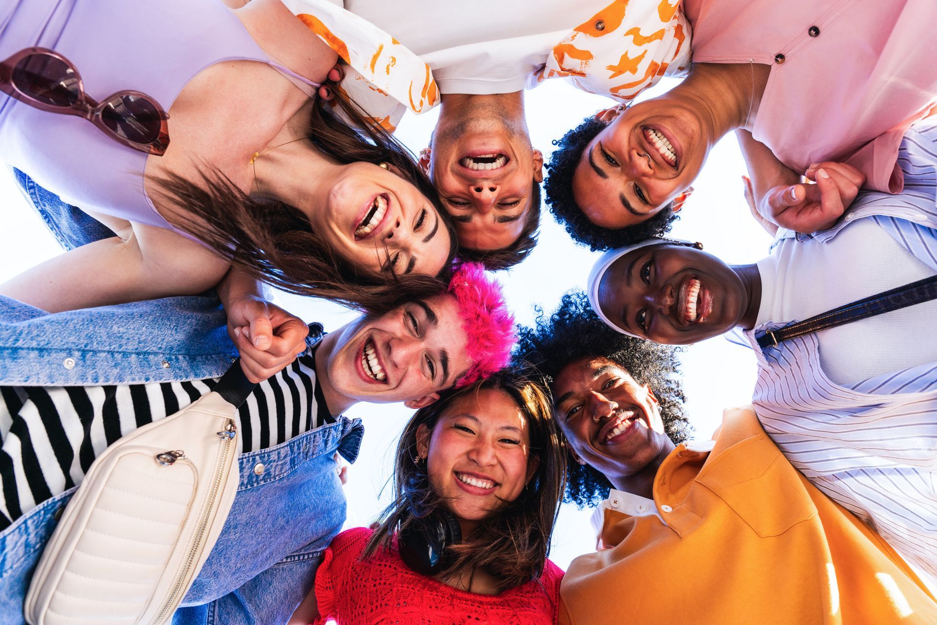 Smiling group of friends lying in a circle with heads together, colorful clothes, viewed from below